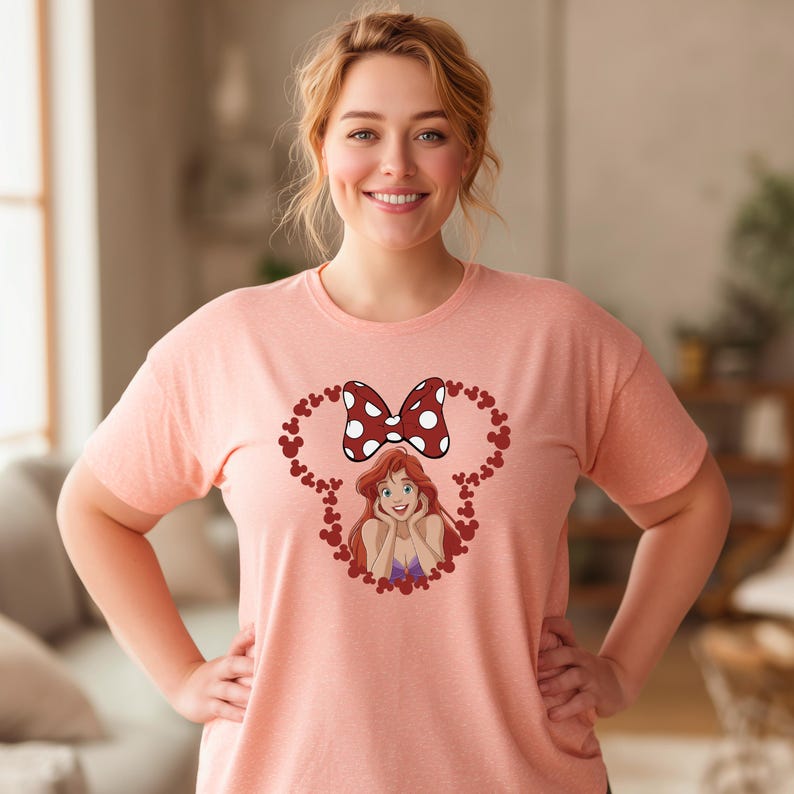 A woman wearing a pink t-shirt with a cartoon character and a bow on it, smiling at the camera.