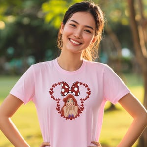 A young woman wearing a pink t-shirt with a cartoon character and a bow on it, smiling at the camera.