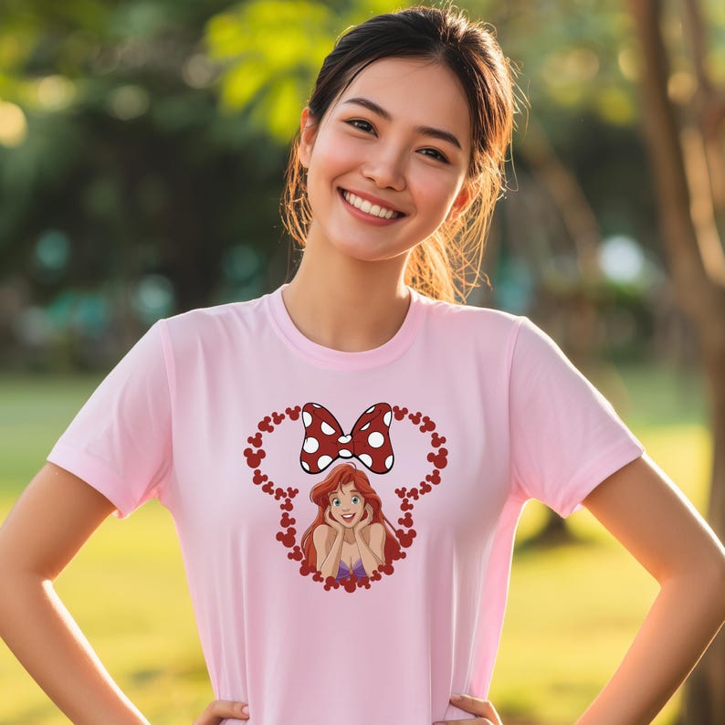 A young woman wearing a pink t-shirt with a cartoon character and a bow on it, smiling at the camera.