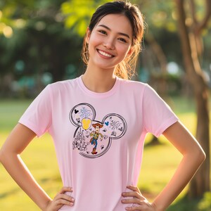 A young woman wearing a pink t-shirt with a Mickey Mouse design is smiling and posing outdoors.