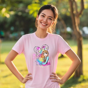 A smiling woman wearing a pink t-shirt with a cartoon character on it, standing in a park.
