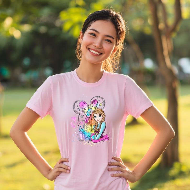 A smiling woman wearing a pink t-shirt with a cartoon character on it, standing in a park.
