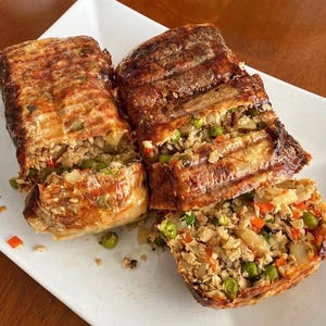 Peut inclure: Deux tranches de pain de viande rectangulaires grillées sur une assiette carrée blanche. Le pain de viande présente un extérieur doré avec des marques de gril et une farce composée de petits pois verts, de carottes orange et d'oignons blancs.