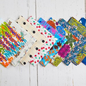 May include: A collection of colorful fabric handkerchiefs with various patterns, including floral, polka dots, and abstract designs. The handkerchiefs are arranged diagonally on a white wooden surface, showcasing a variety of colors and styles.