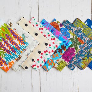 May include: A collection of colorful patterned fabric squares arranged diagonally. Designs include floral, polka dots, cherries, and abstract patterns in various colors like blue, green, orange, and pink. The fabric is displayed on a white wooden surface.