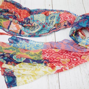 Könnte beinhalten: Ein farbenfroher Schal mit Patchwork-Design. Der Schal zeigt eine Vielzahl von Mustern in Rot-, Blau-, Gelb- und Rosatönen. Quasten sind an den Enden des Schals befestigt.