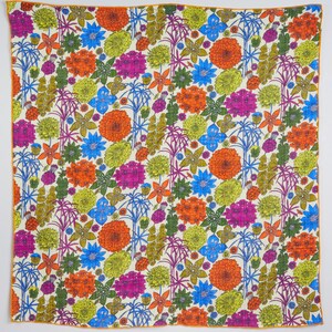 May include: A square textile with a vibrant floral pattern. The design features orange, pink, blue, and yellow flowers, along with green foliage, set against a cream background. The edges are trimmed with a thin orange border.