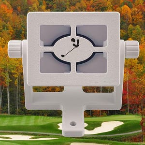 Puede incluir: Un dispositivo blanco de medición de distancia de campo de golf con un gráfico de palo de golf y pelota. El dispositivo tiene un marco cuadrado con perillas ajustables y una base de montaje. El fondo presenta un campo de golf y follaje de otoño.