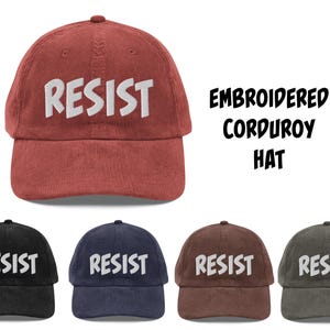 May include: A rust-colored corduroy hat with the word "RESIST" embroidered in white. The image also shows the hat in black, navy, brown, and olive green. Text on the right reads "EMBROIDERED CORDUROY HAT."