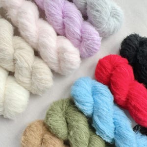 May include: A selection of colourful yarn skeins in shades of white, pink, purple, grey, red, blue, green, and brown. The yarn has a soft, fluffy appearance, suitable for knitting or crochet projects.