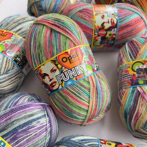 May include: A collection of colourful yarn skeins, labelled "FUNKY". The yarn is a blend of green, pink, red, and blue. The label features a woman's face. Each skein weighs 100g.