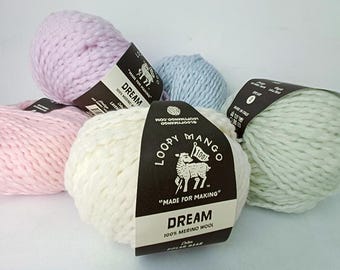 May include: A collection of Loopy Mango Dream yarn in various pastel colors, including pink, lavender, blue, and off-white. Each skein has a black label with the brand logo and text that reads "DREAM 100% MERINO WOOL".