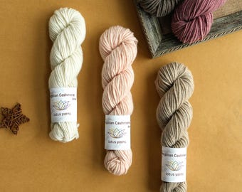 May include: Five skeins of Mongolian Cashmere yarn by Lotus Yarns in cream, pale pink, beige, dark brown, and mauve. Each skein features a white paper label with the text Mongolian Cashmere and the Lotus Yarns logo, a stylized lotus flower.