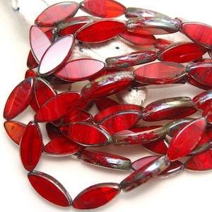 May include: A collection of red glass beads, each with an oval form. The beads are strung together, displaying a glossy surface and a metallic edge. The beads are a rich, deep red colour.