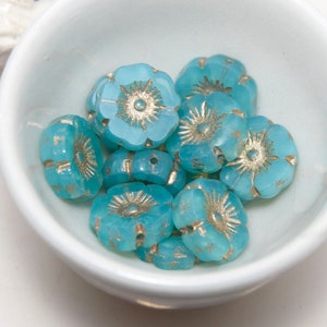 Könnte beinhalten: Eine Schale mit blauen Glasblumenperlen mit silbernen Akzenten. Die Perlen haben die Form von Blumen mit fünf Blütenblättern und einem Kreis in der Mitte.