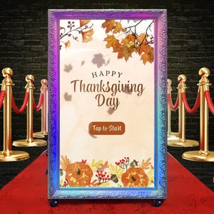 May include: A photo booth with a decorative frame and the text "Happy Thanksgiving Day." The booth features a red carpet and stanchions with velvet ropes. The frame has a fall-themed design with pumpkins and leaves.