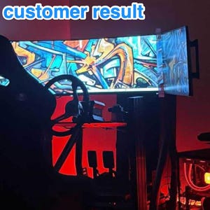 May include: A gaming setup featuring a black racing-style chair, a steering wheel, and a monitor displaying colorful graffiti art. The text "Actual customer result" is visible. The room is illuminated with red lighting, creating a dynamic atmosphere.