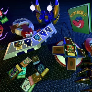 May include: A collection of Yu-Gi-Oh! themed items, including a dice, a card game deck, a book titled "Toon World", and various cards. The items are arranged on a textured, dark blue surface, with a futuristic aesthetic.