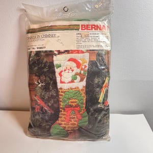 May include: A Bernat Santa in Chimney needlepoint kit in a clear plastic bag. The package features a printed image of a finished Christmas stocking with a Santa Claus figure, a green wreath, and a red bow on a brick-patterned background.