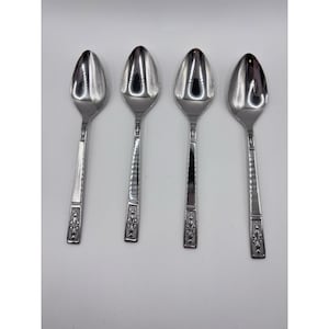 Puede incluir: Cuatro cucharas de acero inoxidable con superficie reflectante. Las cucharas tienen un cuenco en forma de lágrima y un mango decorativo con diseño floral. Los mangos tienen un diseño texturizado y acanalado. Las cucharas están dispuestas verticalmente.