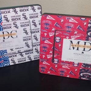 May include: Two rectangular picture frames featuring sports team logos. The left frame displays blue Chicago Cubs and white Chicago Sox patterns. The right frame shows red Philadelphia Phillies and navy Atlanta Braves logos. Both contain MDC inserts.