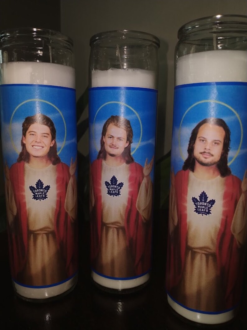 May include: Three glass candle jars with blue and white labels featuring images of men with long hair and beards. The labels also include the text "Toronto Maple Leafs".