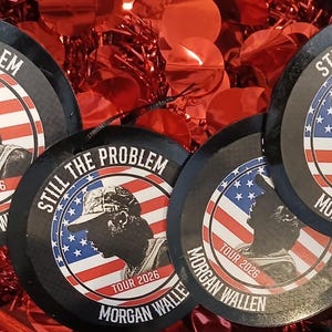 May include: Four circular ornaments featuring a silhouette of a person wearing a baseball cap against an American flag background. The text reads STILL THE PROBLEM, TOUR 2026, and MORGAN WALLEN in black and white lettering on the border.