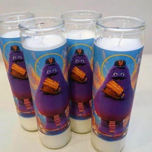 May include: Four glass jar candles with a purple character holding a baseball glove. The character wears a baseball cap with a logo. The background is blue with clouds. The candles have white wax.