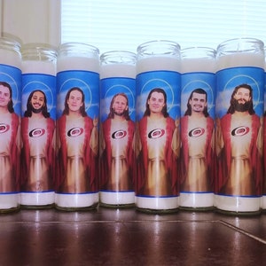 May include: Eight white candles with images of hockey players dressed as Jesus. Each candle features a different player wearing a red and black jersey with a white logo. The candles are arranged in a row on a wooden surface.