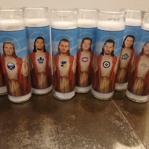 May include: Eight white candles with images of hockey players wearing jerseys of different teams. The players are depicted as Jesus Christ with halos and robes. The teams represented are the Boston Bruins, the Washington Capitals, the Tampa Bay Lightning, the Montreal Canadiens, the Toronto Maple Leafs, the Dallas Stars, the Philadelphia Flyers, and the Chicago Blackhawks.