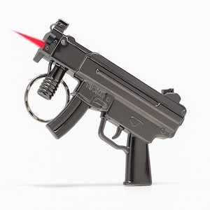 Op de afbeelding: Een donkergrijze metalen sleutelhanger in de vorm van een machinepistool, met een rode laserstraal die uit de loop komt. De sleutelhanger heeft een ring om sleutels aan te bevestigen. Witte achtergrond.