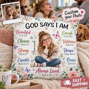 May include: A square white throw pillow featuring a central photograph of a young person with glasses wearing a patterned sweater. The text reads GOD SAYS I AM, Hannah, and lists inspirational words with Bible verses, surrounded by floral art.