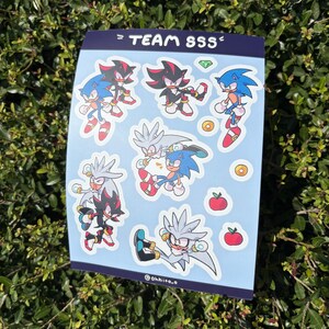 May include: A sticker sheet featuring cartoon characters Sonic, Shadow, and Silver. The characters are in various action poses, with a light blue background. The text "= TEAM SSS =" is at the top.