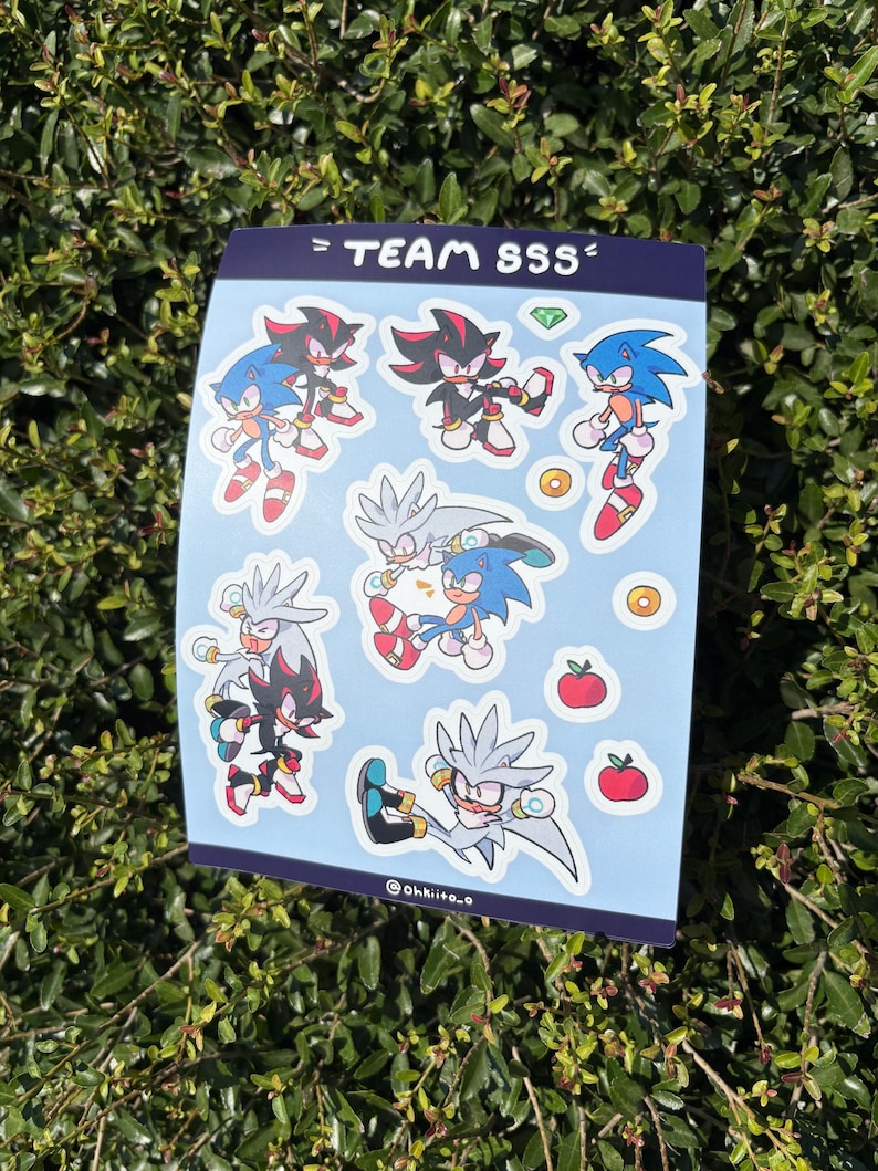 May include: A sticker sheet featuring cartoon characters Sonic, Shadow, and Silver. The characters are in various action poses, with a light blue background. The text "= TEAM SSS =" is at the top.