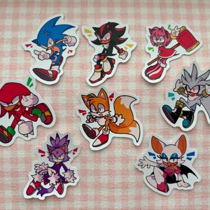 Puede incluir: Un conjunto de ocho pegatinas coloridas con personajes de la serie de videojuegos Sonic the Hedgehog. Las pegatinas representan a Sonic, Shadow, Amy, Knuckles, Tails, Silver, Blaze y Rouge en poses dinámicas, con colores vibrantes y diseños detallados.