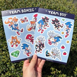 May include: Two sticker sheets featuring cartoon characters from the Sonic the Hedgehog franchise. One sheet is labeled "TEAM SONIC" and the other "TEAM SSS". The stickers depict Sonic, Tails, Knuckles, Shadow, and Silver.