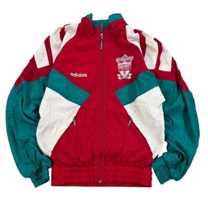 Könnte beinhalten: Vintage Adidas Liverpool FC Trainingsjacke in Rot, Weiß und Türkis. Die Jacke hat einen durchgehenden Reißverschluss, das Adidas-Logo und das Liverpool FC-Wappen. Türkisfarbene und weiße Einsätze akzentuieren die Ärmel und Schultern.