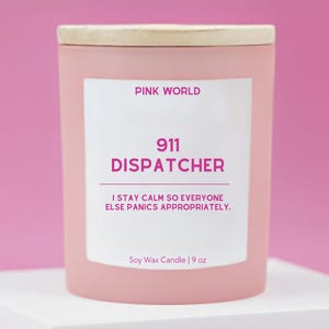 May include: A pink soy wax candle with a wooden lid. The label reads "PINK WORLD", "911 DISPATCHER", and "I STAY CALM SO EVERYONE ELSE PANICS APPROPRIATELY." The candle is 9 oz.