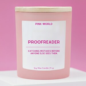 May include: A pink soy wax candle with a wooden lid. The label reads "PINK WORLD" and "PROOFREADER", with the tagline "CATCHING MISTAKES BEFORE ANYONE ELSE SEES THEM." The candle is 9 oz.