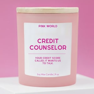 May include: A pink soy wax candle with a wooden lid. The label reads "PINK WORLD CREDIT COUNSELOR YOUR CREDIT SCORE CALLED. IT WANTS US TO TALK." The candle is 9 oz.
