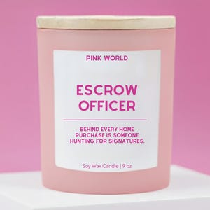 May include: A pink soy wax candle with a wooden lid. The label reads "PINK WORLD ESCROW OFFICER" with the text "BEHIND EVERY HOME PURCHASE IS SOMEONE HUNTING FOR SIGNATURES." The candle is 9 oz.