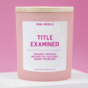 May include: A pink soy wax candle with a wooden lid. The label reads "PINK WORLD TITLE EXAMINER DIGGING THROUGH HISTORY SO YOU DON'T INHERIT PROBLEMS." The candle is 9 oz.
