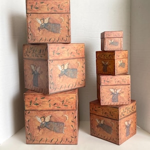 May include: A collection of decorative boxes in varying sizes. Each box is a warm, earthy tone with a painted angel design and a crescent moon. The boxes are adorned with a leafy vine pattern around the edges, creating a cohesive set.