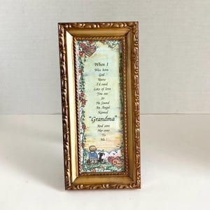 May include: A framed print with a gold-colored ornate frame. The print features a poem with the word "Grandma" in the center. The artwork includes illustrations of a child, a dog, and floral accents.