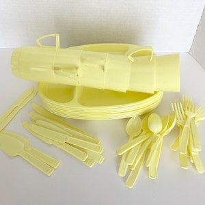 May include: A collection of pale yellow plastic picnic tableware. Includes plates, cups, knives, forks, spoons, and serving utensils. The plates have divided sections. The cups have handles. The utensils are all the same color.
