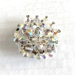 May include: A vintage clear crystal brooch with iridescent accents. The brooch is round, composed of multiple clear, faceted crystal beads, and has silver-tone metal accents. The crystals reflect light, creating a sparkling effect. This jewelry piece is suitable for special occasions.