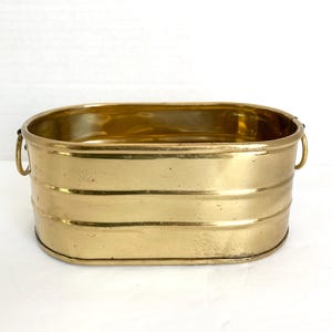 May include: Oval brass planter with two handles. The planter has a smooth, shiny finish and is made of solid brass.
