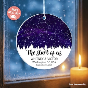 May include: A round, white ceramic ornament with a starry night design. The ornament features a deep purple sky with constellations and the text "The start of us," along with names, location, and a date.