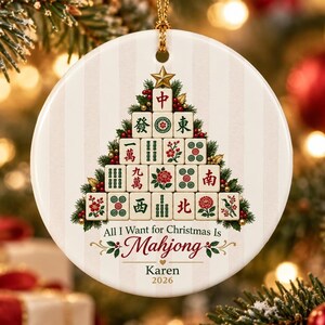 May include: A round white ceramic ornament featuring a Christmas tree graphic constructed from Mahjong tiles. The text reads All I Want for Christmas Is Mahjong, with the name Karen and the year 2026 printed below in black lettering.
