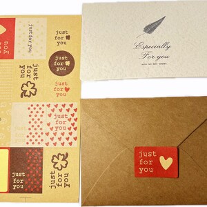 May include: A collection of stationery items, including stickers, cards, and an envelope. The stickers feature the text "just for you" with heart and clover designs. One card has the text "Especially For you" and a feather illustration. The envelope has a red sticker with a heart.